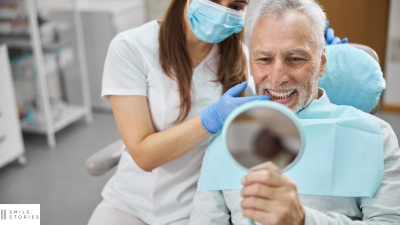 an elderly man with grey hair sat in a dental chair looking at his dental implants Dorchester