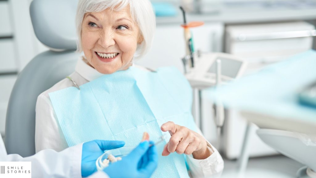 white female with grey hair sat in a dental chair. dentist is holding denture implants