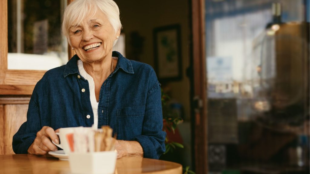 older female with white hair drinking coffee in a coffee shop Salisbury. She has a dental implant